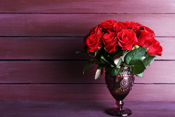 Bouquet of red roses in glass vase on wooden background