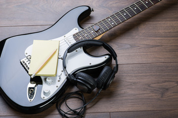 Naklejka premium Black electric guitar with notepad, headphones and pencil