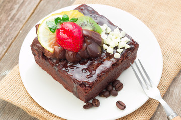 Piece of chocolate cake with icing and fresh berry on wooden bac