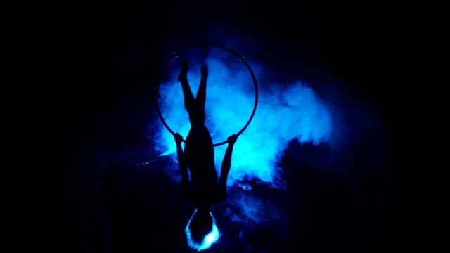 Aerial acrobat woman on circus stage. Silhouette on a blue