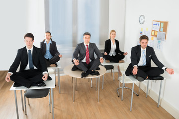 Meditating Businesspeople Sitting On Desk