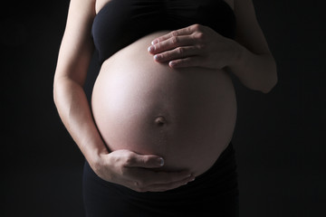A belly of a pregnant woman on the black background