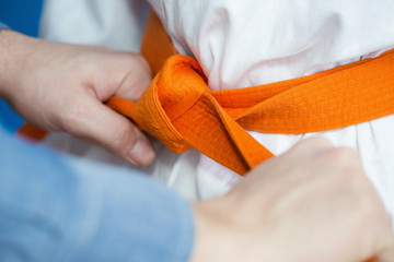 Vader knoopt een oranje riem aan het vechtsportuniform van zijn zoon