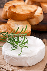 Camembert cheese and a sprig of rosemary on a wooden table