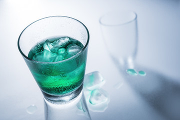Glass of green drink with ice on a glass table.