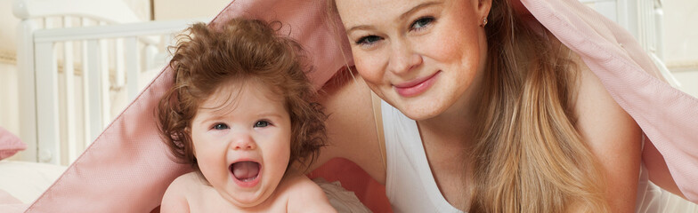 Mother and baby playing and smiling under a blanket. Happy famil