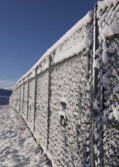 Chain-link fence line covered in snow with blue sky