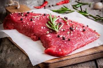 raw meat steak on a cutting board with rosemary and red pepper