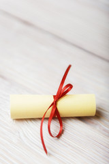 Rolled paper with red ribbon on white vintage wooden background