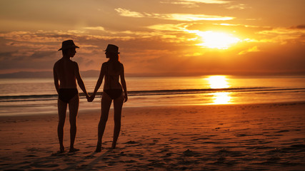 Pretty couple is standing on the tropical sunset background