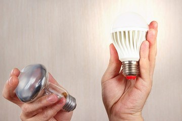 Hands compared incandescent bulb and glowing led lamp