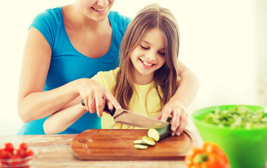 Obraz na płótnie Canvas smiling little girl with mother chopping cucumber