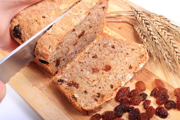 Slicing fresh bread, ears of wheat and raisins