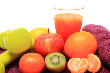Fresh fruits, glass of juice and dumbbells on purple towel