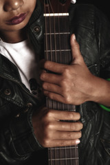Girl rocker in leather jacket holding a guitar in his hands