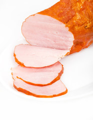 Large piece of ham with cut slices on plate, isolated on white b
