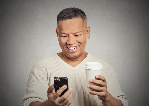 Happy man looking at mobile cell phone holding cup coffee