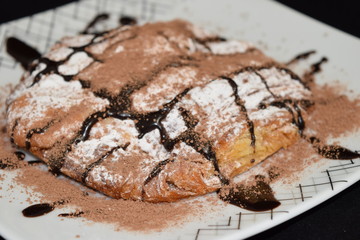 Croissant with powder sugar and melted chocolate on it.