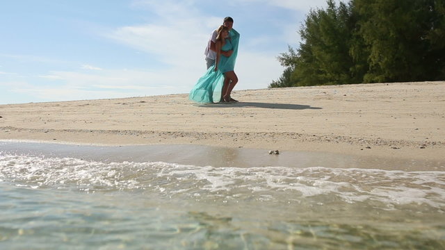 handsome guy embraces and kisses blonde girl on sand beach