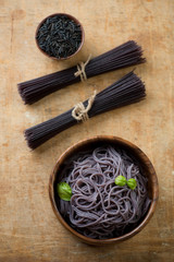 Cooked and raw black rice noodles over rustic wooden surface
