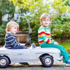 Two happy twins playing with big old toy car in summer garden, o