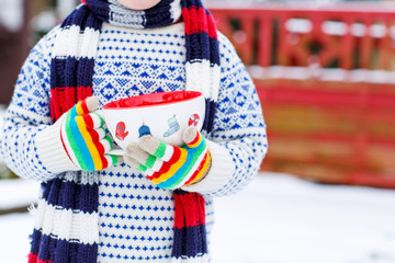 Hands of little child holding big cup with snowflakes and hot ch