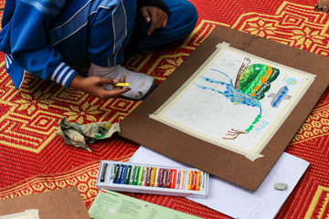  The asian boy is painting crayon color on her drawing for drawi