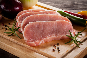 Raw pork chops on cutting board and vegetables