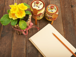 Notebook with a pencil on a wooden table with yellow primroses a