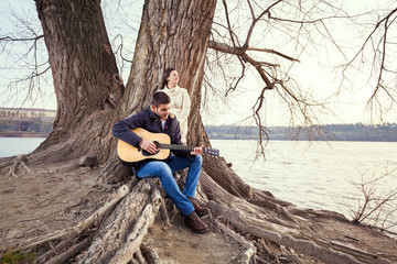 Young couple sitting on a tree and playing guitar