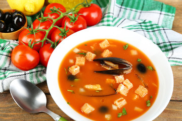 Tasty soup with mussels, tomatoes and black olives in bowl