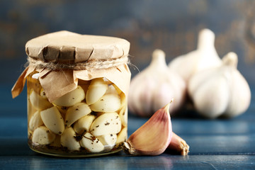 Canned garlic in glass jar on color wooden background