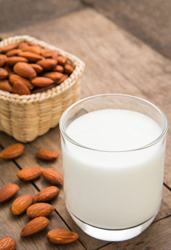 Almond milk in glass with almonds on wooden table