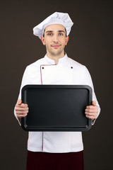 Portrait of chef with oven pan in hands on dark background