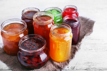 Homemade jars of fruits jam on color wooden planks background
