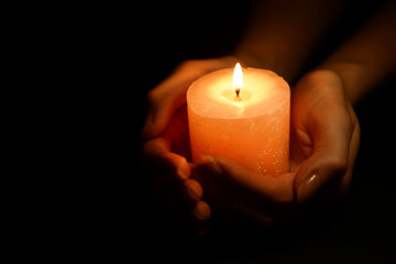 Candle in female hands on black background