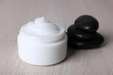 Cosmetic cream with spa stones on wooden background