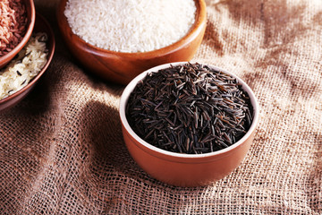 Different kinds of rice in bowls on sackcloth background
