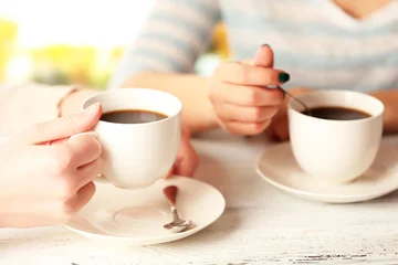 Fotobehang Two women with cups of coffee on bright background © Africa Studio