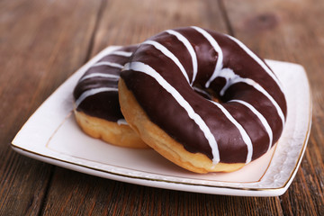 Delicious donuts with icing on plate on wooden background