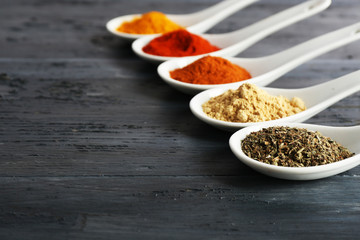 Different kinds of spices in spoons on wooden background