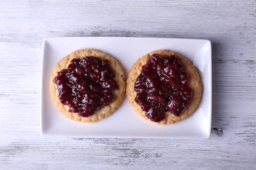 Delicious cookies with jam on plate on wooden background