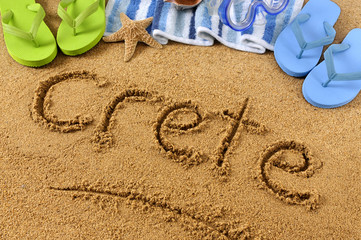 The word Crete written in sand on a beach with towel flip flops seashells Greek Islands summer...