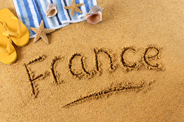 Fototapeta na wymiar The word France written in sand on a beach with towel flip flops seashells summer vacation holiday photo
