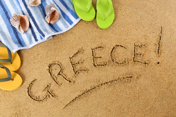Fototapeta na wymiar The word Greece written in sand on a beach with towel flip flops seashells summer vacation holiday photo