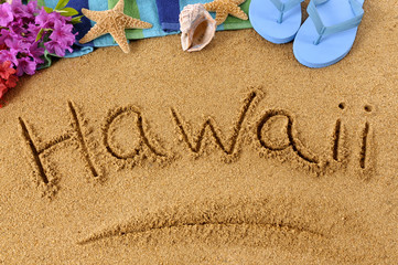 Fototapeta na wymiar The word Hawaii written in sand on a beach with towel flip flops seashells Hawaiian summer vacation holiday photo