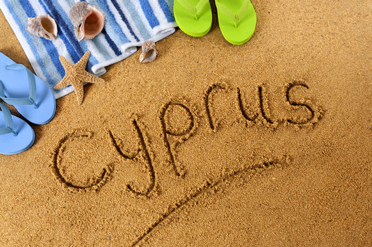 The word Cyprus written in sand on a beach with towel flip flops seashells summer vacation holiday photo