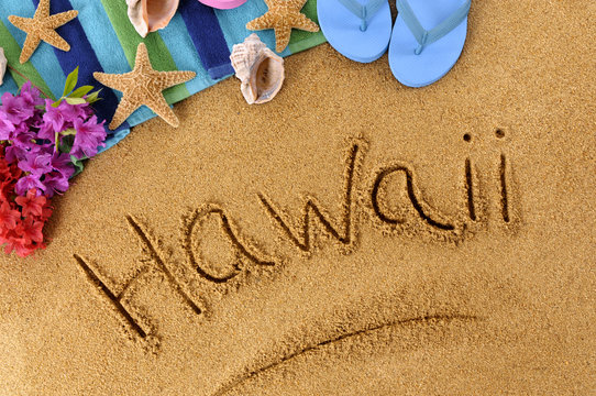 The word Hawaii written in sand on a beach with towel flip flops seashells Hawaiian summer vacation holiday photo