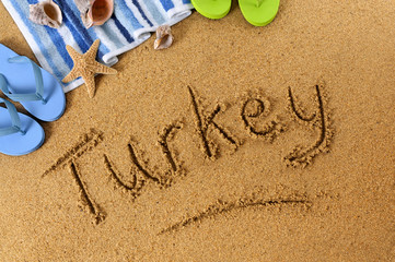 Fototapeta na wymiar The word Turkey written in sand on a beach with towel flip flops seashells summer vacation holiday photo