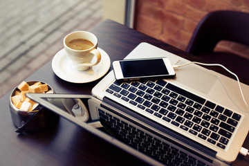 Laptop with phone connected to wire and cup of coffee on a table